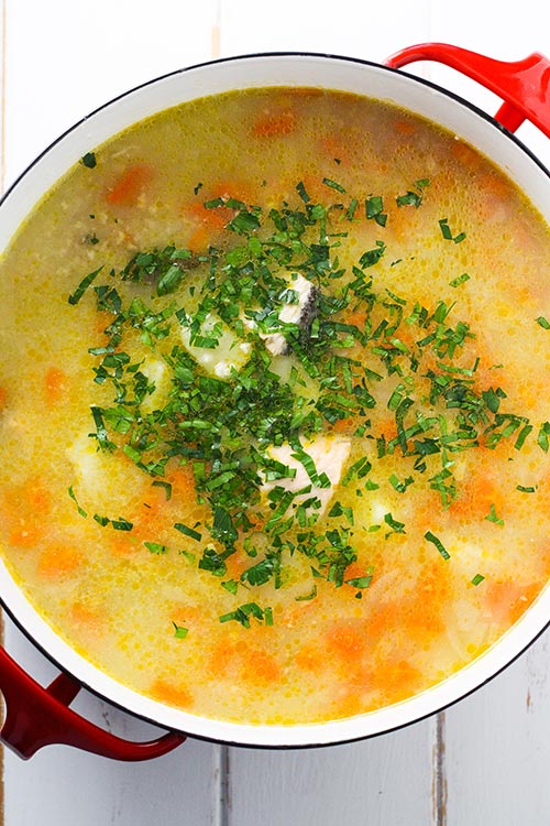 Overhead view of a pot of Ukha, Russian fish soup. Fish is gently cooked with potatoes and carrots in a rich broth seasoned with bay and black pepper. 